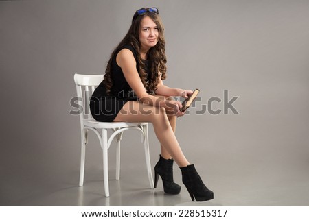 brunette with long hair in black dress sits on white chair