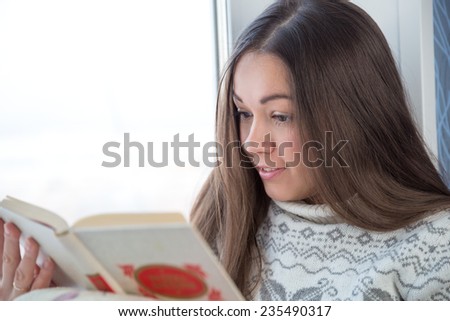 Surprised girl in sweater sitting on the window sill and reading book