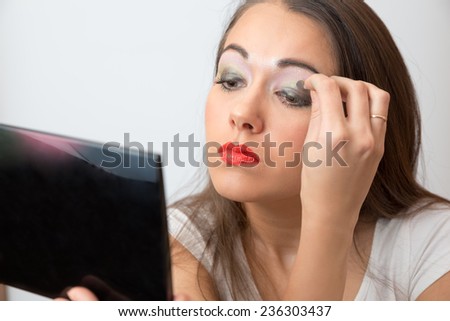 Young woman color eye shadows look in the mirror on white background