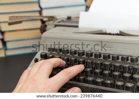 man\'s hand on an old typewriter on background of a pile of books
