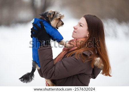 redhead girl in  bright scarf keeps  dog in blue overalls on hand