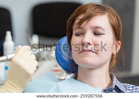 Girl with suspicion looks at drill in  hands of  dentist