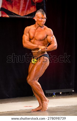 Izhevsk, Russia - April 18, 2015. Open championship of the Volga Federal District of bodybuilding and fitness bikini. sun- tanned bodybuilder with mohawk shows biceps