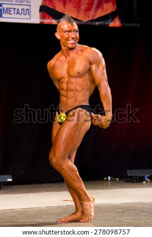 Izhevsk, Russia - April 18, 2015. Open championship of the Volga Federal District of bodybuilding and fitness bikini. sun- tanned bodybuilder with mohawk shows triceps