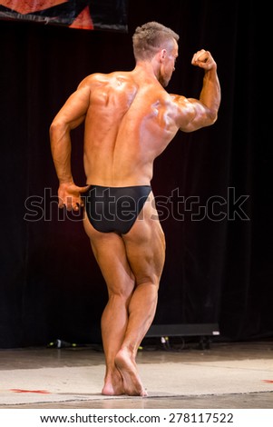 Izhevsk, Russia - April 18, 2015. Open championship of the Volga Federal District of bodybuilding and fitness bikini. Sun-Tanned Bodybuilder in black briefs  showing double biceps during performances