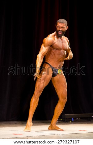 Izhevsk, Russia - April 18, 2015. Open championship of the Volga Federal District of bodybuilding and fitness bikini. Bodybuilder with a beard on the face of aggression and posing on stage