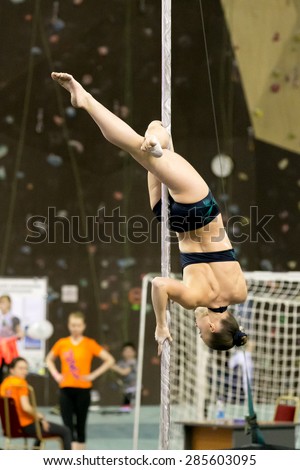 Perm, Russia - April 25, 2015. Championship Perm region at pole sport and dance. Girl in a black swimsuit with a green design makes element Jasmine on rotating pole