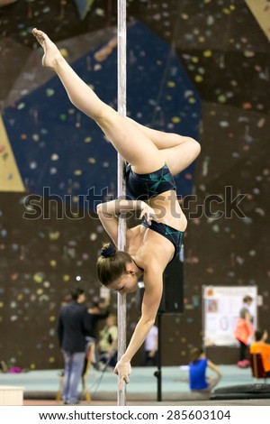 Perm, Russia - April 25, 2015. Championship Perm region at pole sport and dance. Girl in black shorts and top with green design makes element  the hook elbow  upside down
