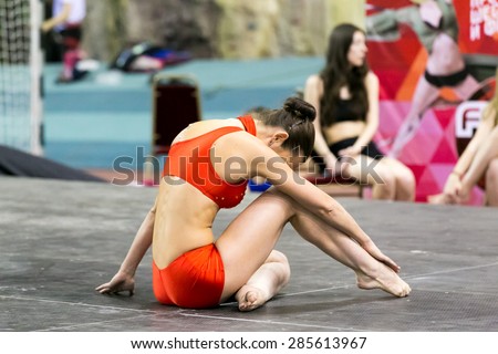 Perm, Russia - April 25, 2015. Championship Perm region at pole sport and dance. brunette in red dance costume sitting on the floor buried in knee
