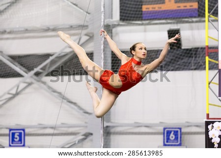 Perm, Russia - April 25, 2015. Championship Perm region at pole sport and dance. young brunette woman in a red dance suit makes element holding a pole