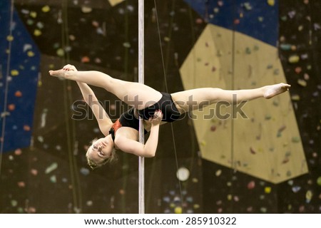 Perm, Russia - April 25, 2015. Championship Perm region at pole sport and dance.  little girl blonde in a black bathing suit makes the element Jamilla split (Jade)