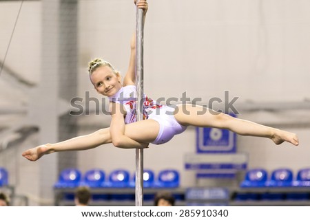 Perm, Russia - April 25, 2015. Championship Perm region at pole sport and dance. Little smiling sportswoman in white swimsuit makes element  Diva onpole split (elbow hold)