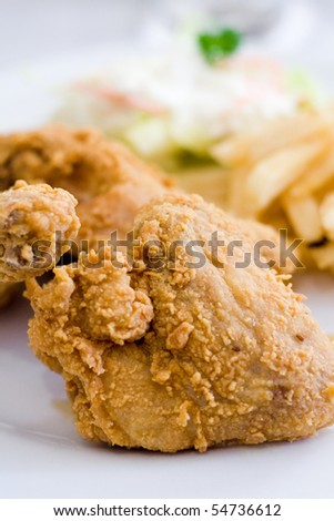 Golden brown deep fried chicken being served on a white plate with fries and salad.