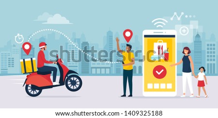 Happy family standing next to their smartphone in the city street, they are receiving a ready fast food meal ordered online using a mobile app, the delivery man is riding a moped