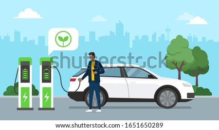 Man charging his electric car at the charging station, city in the background, green energy concept