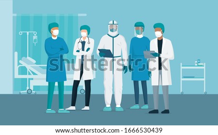 Professional doctors and nurses posing together in a hospital ward and wearing protective suits, virus outbreak emergency concept
