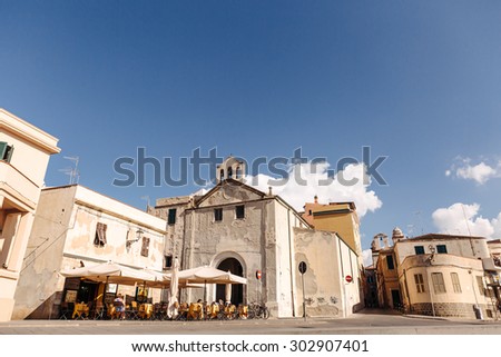 The restaurant is outdoors, under umbrellas with tables and chairs. Cafe on the street. Promenade overlooking the old city in Italy, blue sky, clouds and a pier with boats. In the summer in Sardinia.