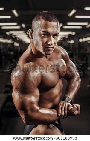 Handsome athletic man power training with dumbbells pumping muscle. Strong bodybuilder six pack, perfect ABS, shoulders, biceps, triceps and chest. Young adult bodybuilder doing weight lifting in gym.