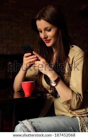 Portrait of young woman sitting relaxed at a cafe drinking coffee and chatting using her cell phone