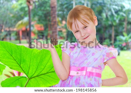 Small blonde girl holding something in his hands on a tropical background