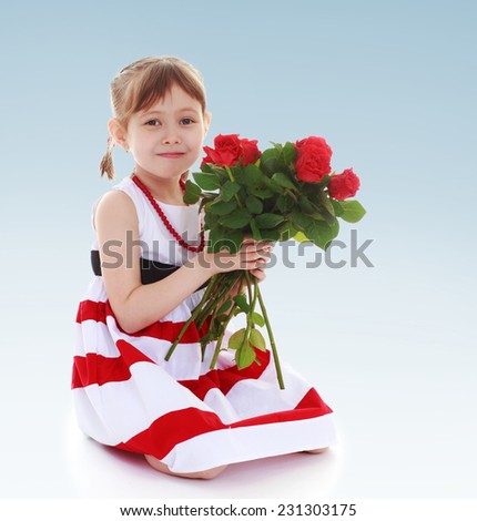 Adorable little girl in a striped dress is holding a large bouquet of red roses.