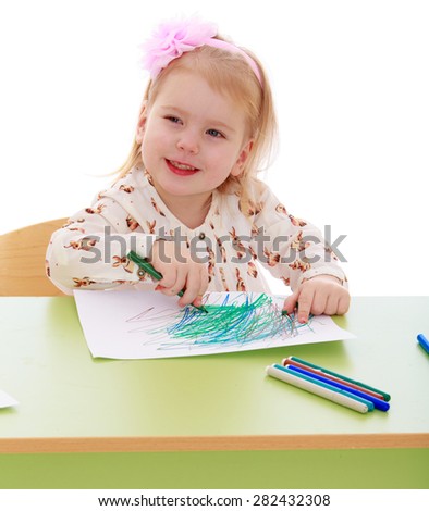 Funny girl draws with markers sitting at the table- isolated on white background