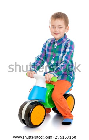 Cheerful blond boy in a plaid shirt and orange jeans riding a plastic bike - isolated on white background