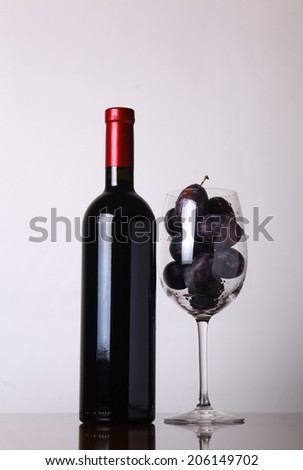 Bottle of red wine with a glass filled with plums over a white background
