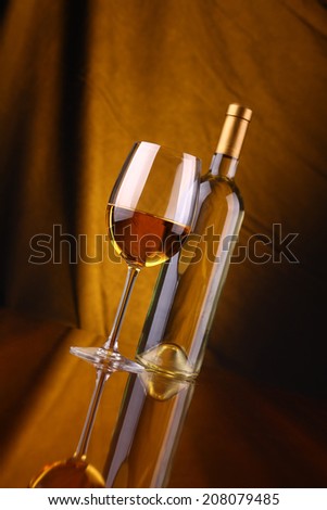 Glass and bottle of white wine over a draped background lit yellow