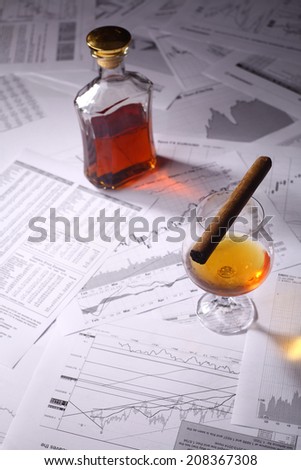 Glass and bottle of brandy with a cigar standing on scattered stock exchange charts