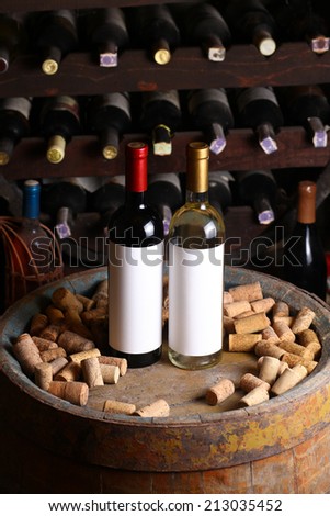Bottles of red and white wine with blank label templates standing in a wine cellar on a wood barrel
