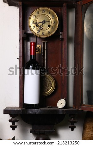 Bottle of red wine with blank label template standing inside an old clock