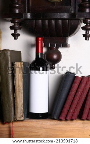 Bottle of red wine with blank label template standing on a shelf with books under an old clock