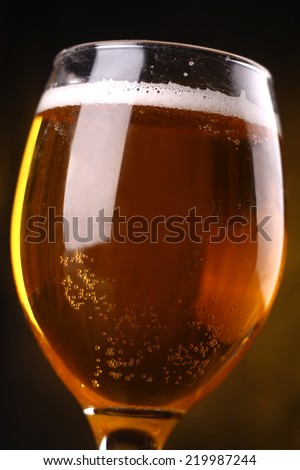 Closeup shot of a glass filled with sparkling light beer with froth over a warm lit background