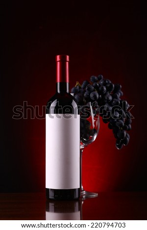 Bottle of red wine with a blank label with a glass filled with ripe grapes over a dark red background