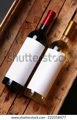 Bottles of red and white wine with blank labels in a wooden crate with grape juice stains