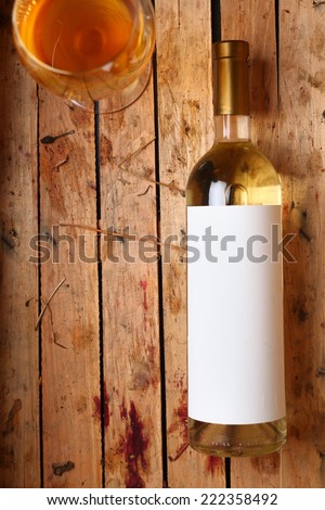 Bottle of white wine with a blank label and a full glass in a used wooden crate with grape juice marks