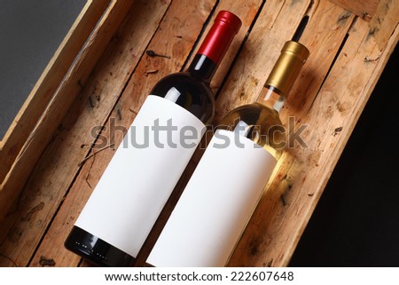 Bottles of red and white wine with blank labels in a wooden crate with grape juice stains