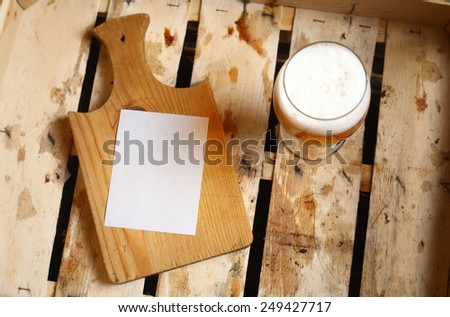 Empty note sheet on a wooden cutting board with full beer glass in a wooden crate