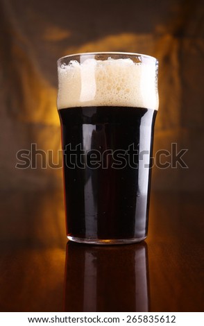 Nonic pint of dark stout beer on a table with a warm colored drapery in the background