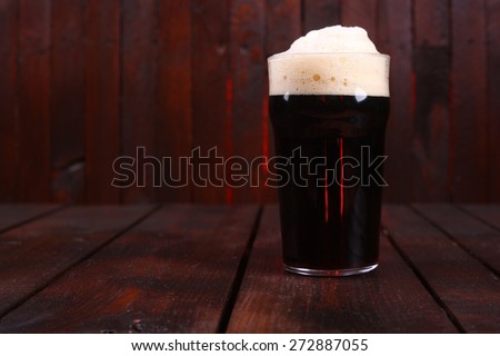 A pint glass full of dark stout ale standing on a wooden table