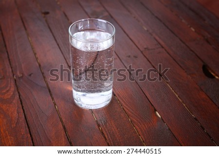 Tall glass full of lightly carbonated drinking water standing on a wooden table