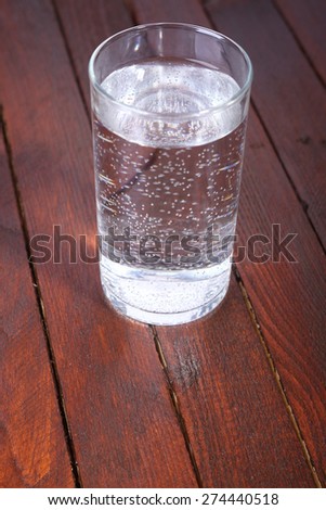Tall glass full of lightly carbonated drinking water standing on a wooden table