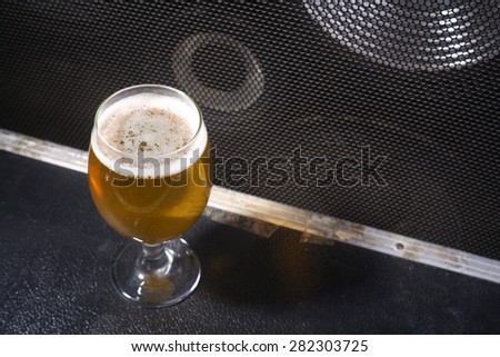 Glass full of light beer standing on a music equipment crate near a big grilled music monitor