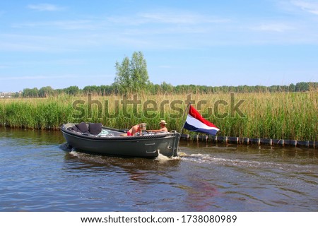 Couple is sailing at river in motor sloop boat with waving Dutch flag, Loosdrechtse Plassen, Loosdrecht, Netherlands  ストックフォト © 