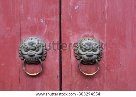Two antique door knockers with animal heads on pink grungy doors in the village Daxu, China