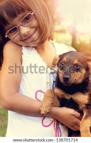 Happy little girl with eye glasses holding her puppy. Warm effect edition.