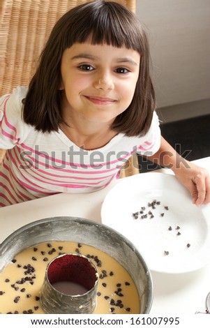 Happy and cute little girl pouring chocolate chips to cake