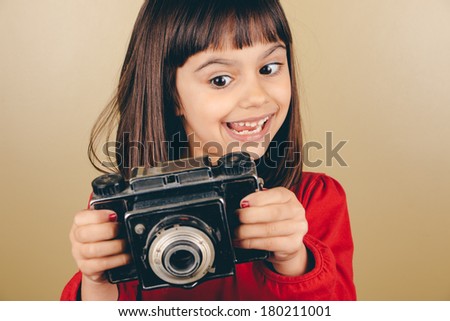Cute little girl holding an old medium format camera with a funny expression. Some film grain and vintage effect added