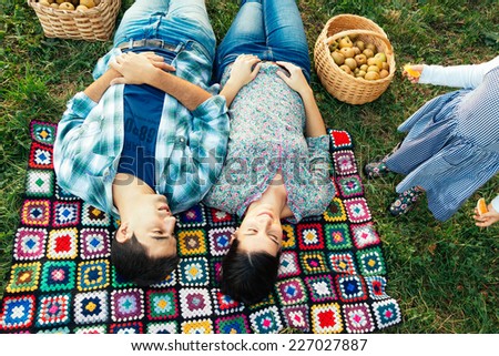 Loving couple resting on a crocheted blanket on the grass in autumn after picking apples. Toddler demands attention. Top view.